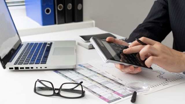 パソコンの前で電卓を操作する人のイメージ