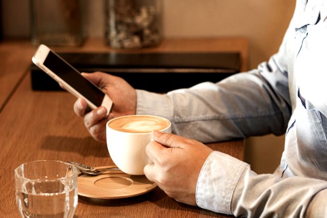 カフェでコーヒーを片手にスマホを操作する男性のイメージ