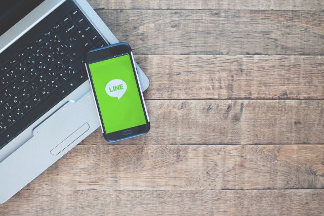 テーブルの上にパソコンとLINEのアプリが表示されたスマホのイメージ