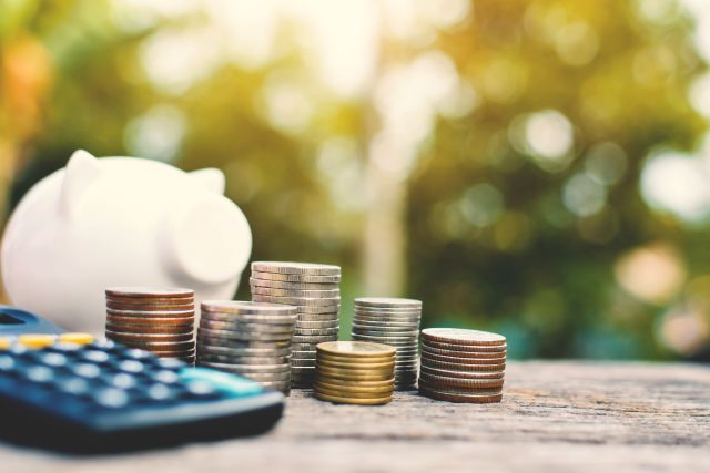 積み上げられた硬貨と電卓・豚の貯金箱のイメージ