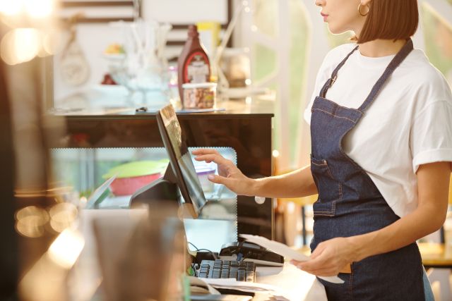 レジのタッチパネル操作を行う女性店員のイメージ
