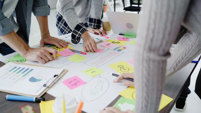 書類やカラフルな付箋が散らばったデスクで話し合う人のイメージ