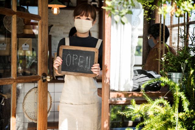 OPENと書かれたボードをもって店頭に立つ女性のイメージ
