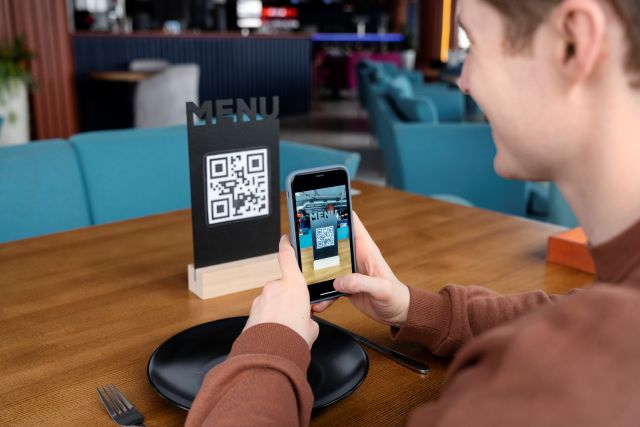 スマホのカメラ機能でテーブル状に設置されたQRコードを読み取る人のイメージ