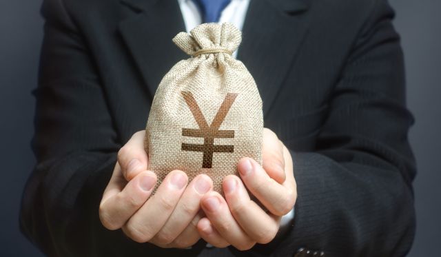 スーツ姿の男性が両手で円マークの入った包みをもつイメージ