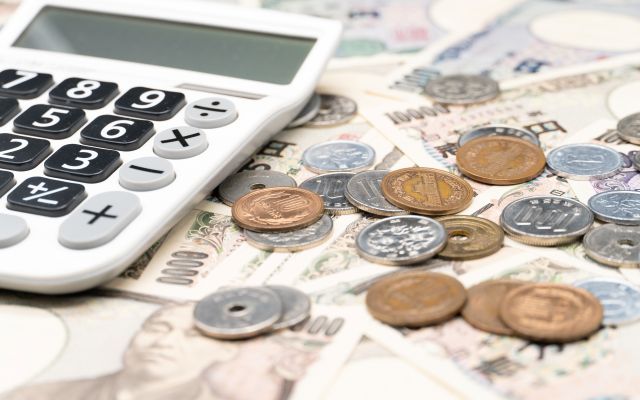 散らばった日本紙幣の上に硬貨と電卓が置かれているイメージ