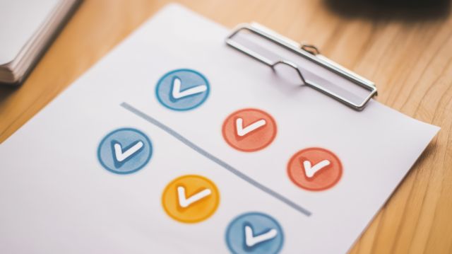 バインダーに挟んだ紙に赤青黄でチェックマークが書かれているイメージ