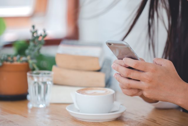 カプチーノが置かれたカフェの席でスマホを操作する人のイメージ
