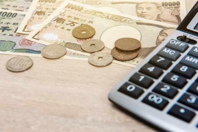 テーブルに散らばった日本の紙幣と硬貨・電卓のイメージ