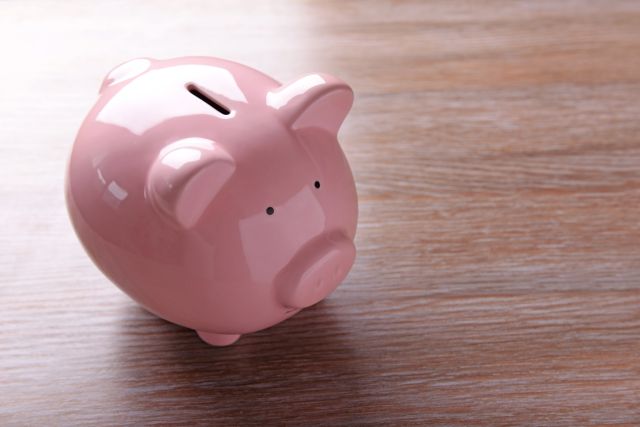 机に置かれた桃色の豚の貯金箱のイメージ