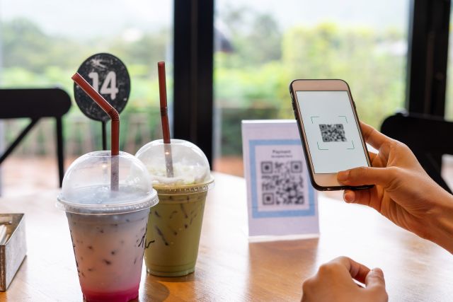 カフェのテーブルでポップのQRコードをスマホで読み取る人のイメージ