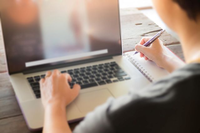 パソコンを見ながらメモを取る人