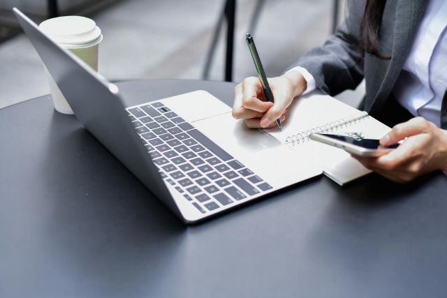 パソコンを見ながらメモを書く人