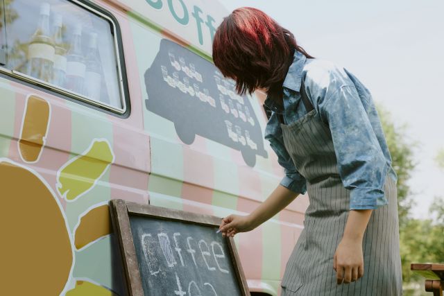 バンタイプのキッチンカーに看板を立てかける女性